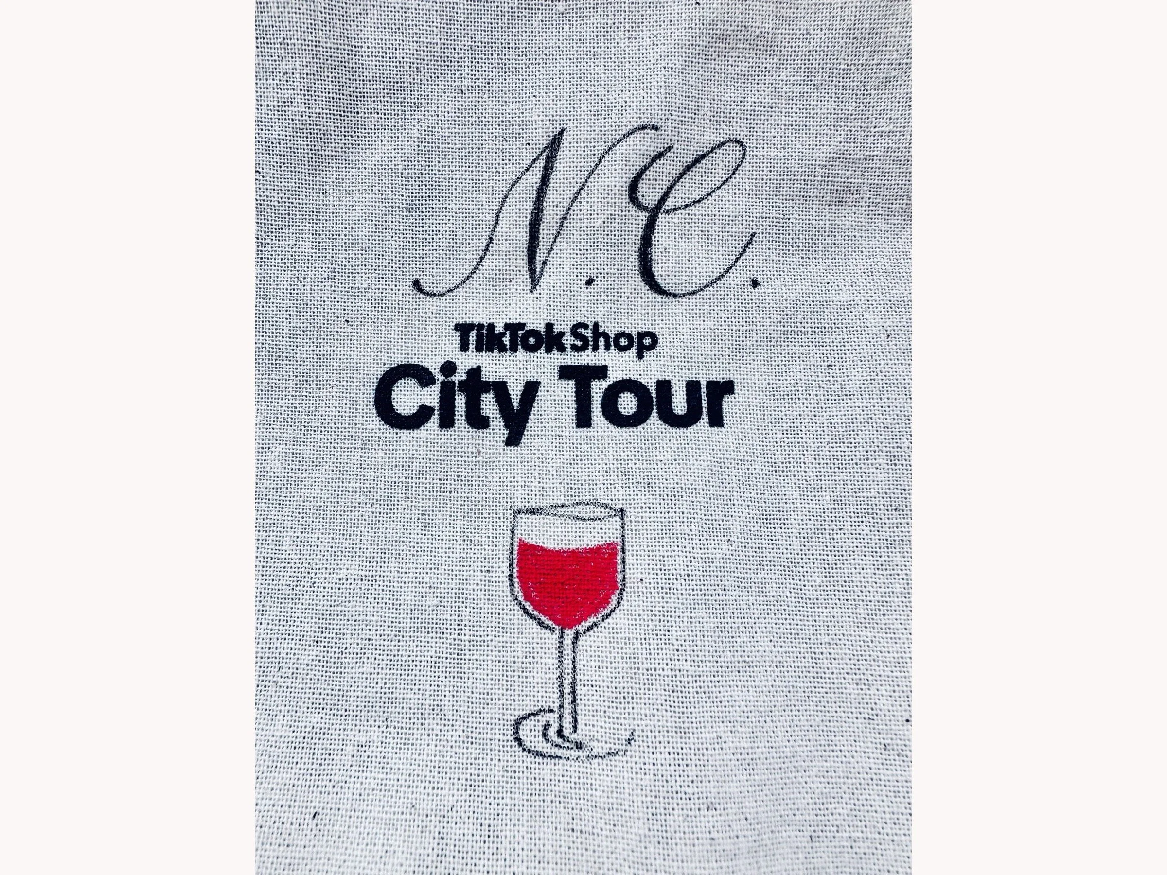 Hand-lettered N.C. monogram in black calligraphy on a TikTok Shop City Tour fabric bag, live calligraphy at a Los Angeles event