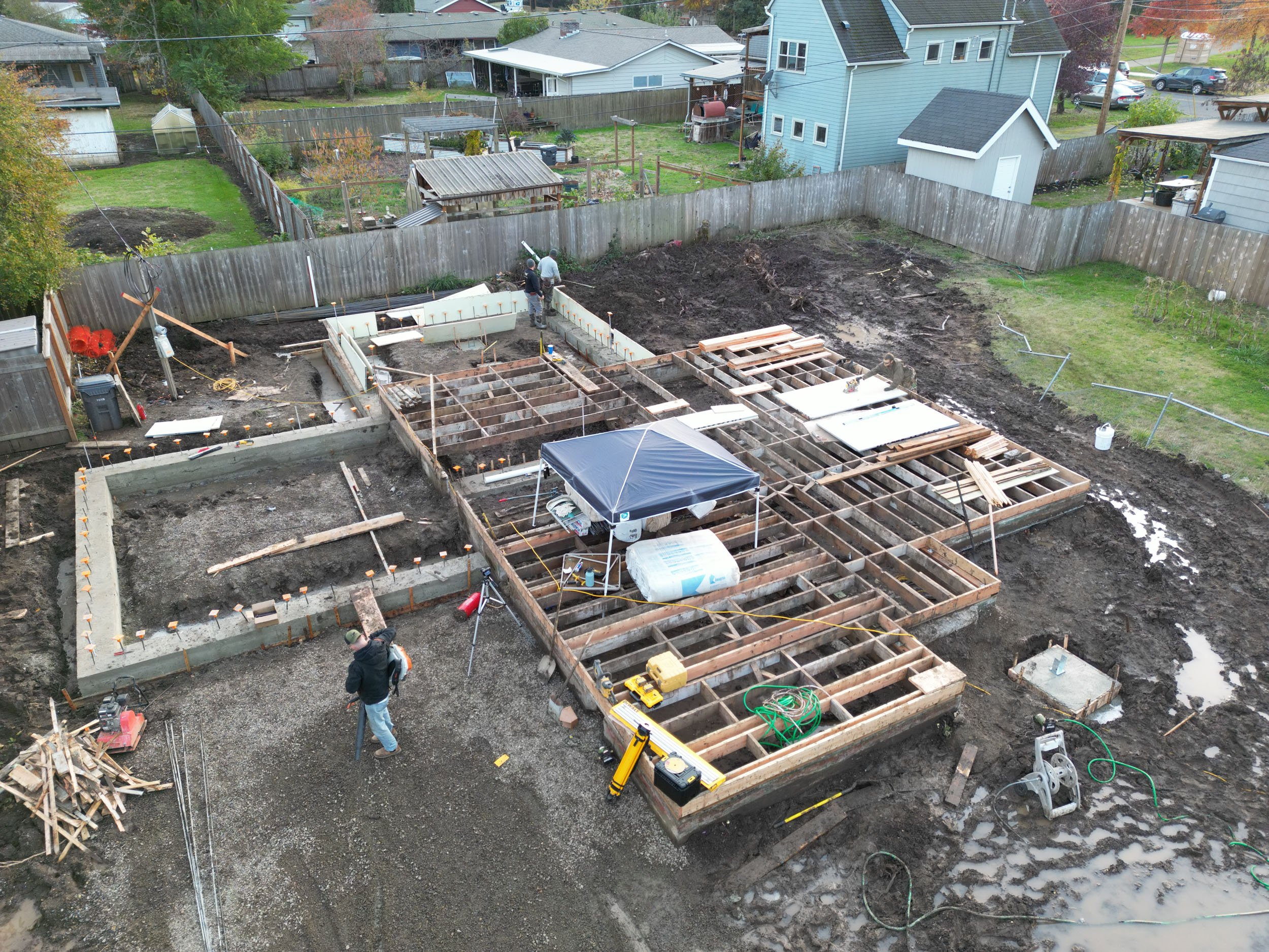 Aerial view of a construction site with foundation and wooden framework, surrounded by residential houses.