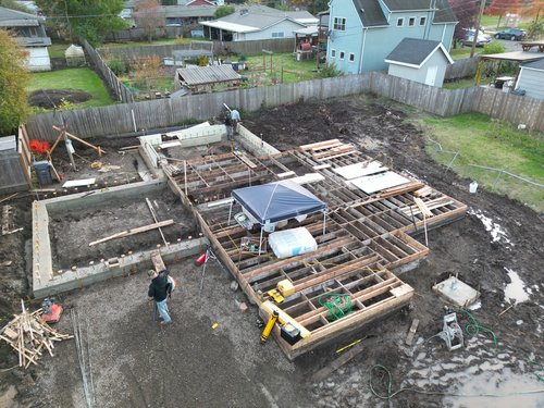 Aerial view of a construction site with foundation and wooden framework, surrounded by residential houses.