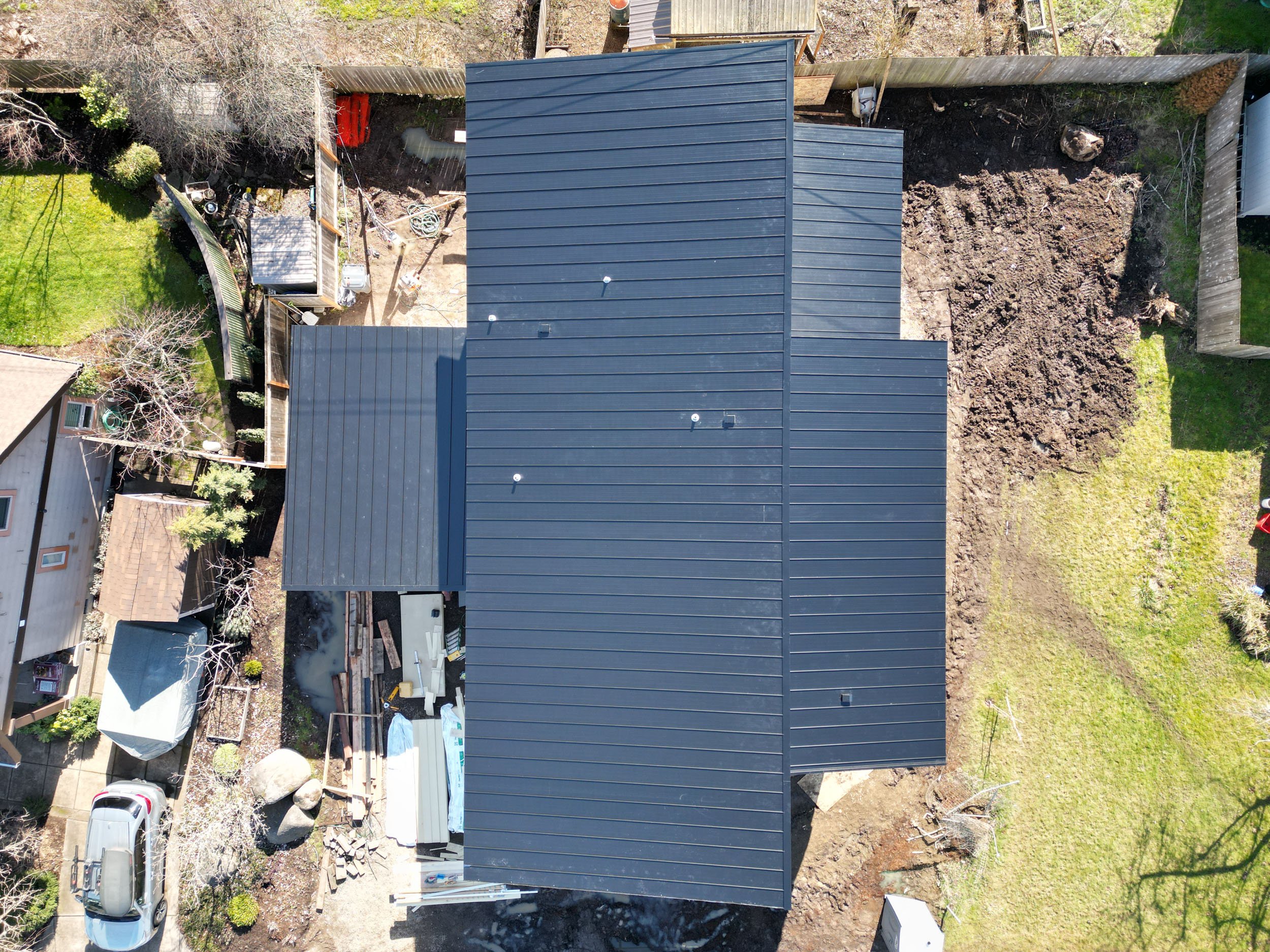 Aerial view of a house with a black metal roof surrounded by a yard and other buildings.