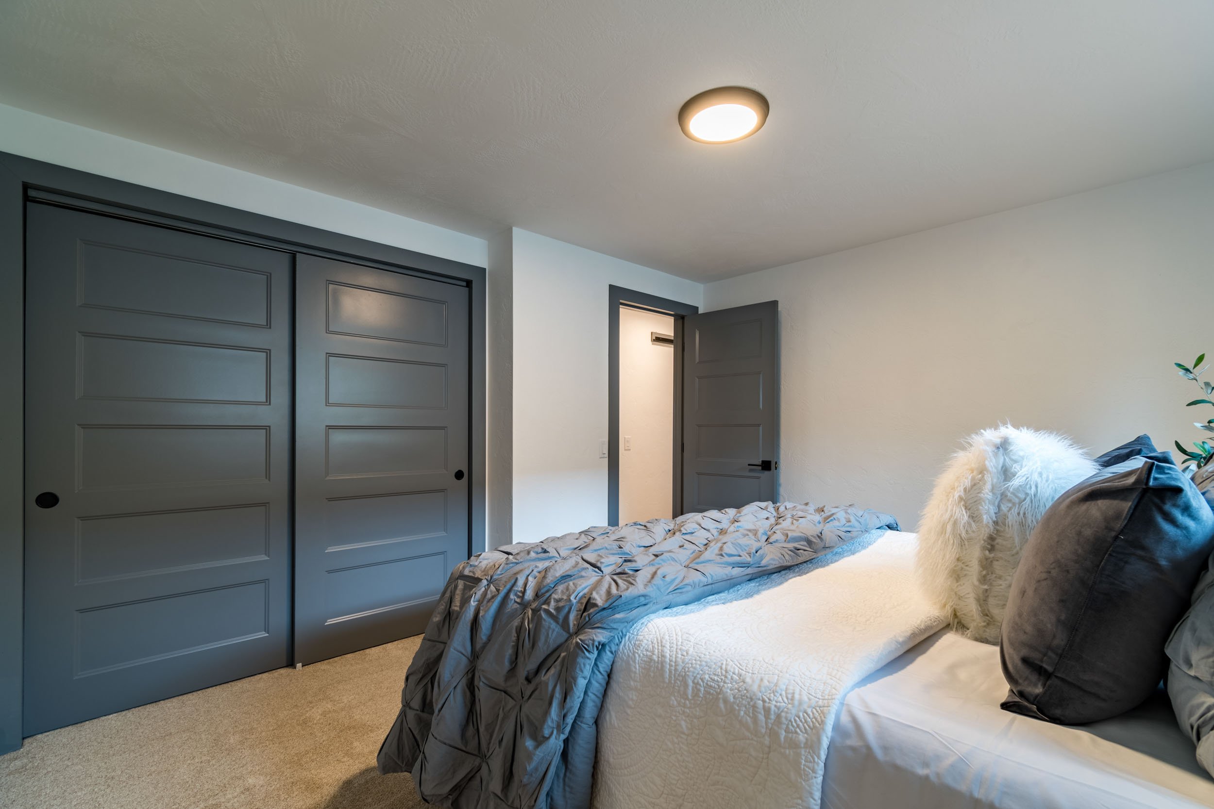 Modern bedroom with gray sliding closet doors, a doorway leading to another room, and a neatly made bed with white and gray bedding and decorative pillows.