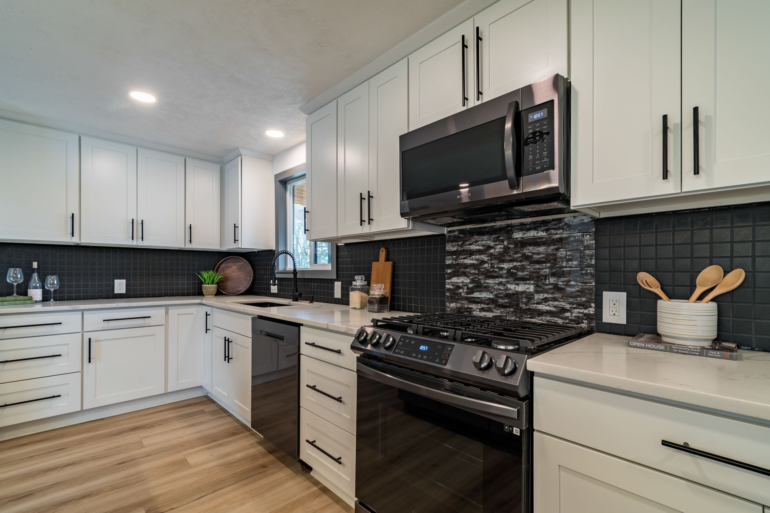 Modern kitchen with white cabinets, stainless steel appliances, black tile backsplash, and wood flooring.