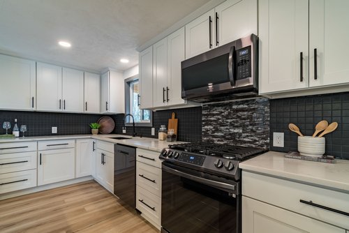 Modern kitchen with white cabinets, stainless steel appliances, black tile backsplash, and wood flooring.