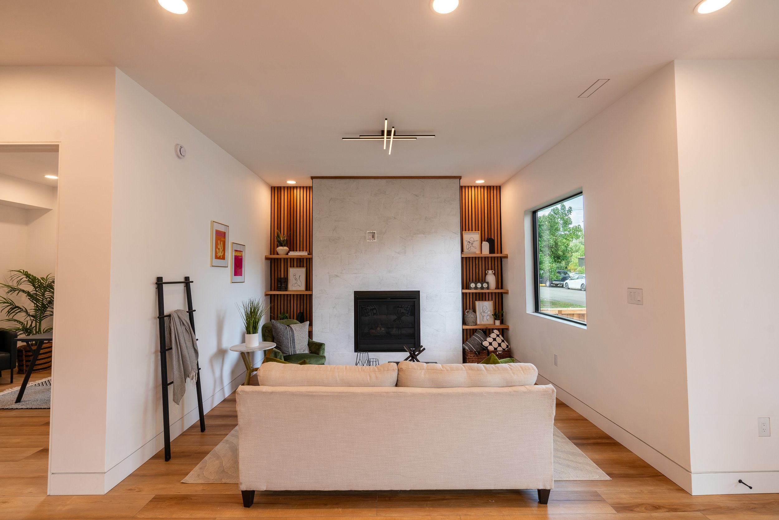 Modern living room with beige sofa, fireplace, shelves, and large window.