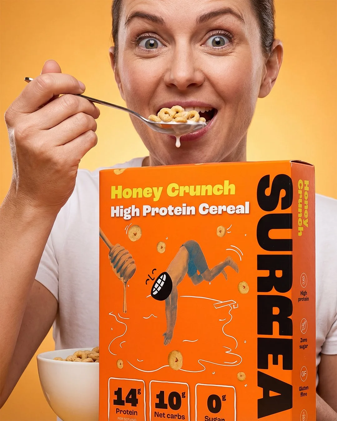 Close-up lifestyle image of a person eating Honey Crunch high protein cereal with the cereal box visible in the foreground against an orange background.