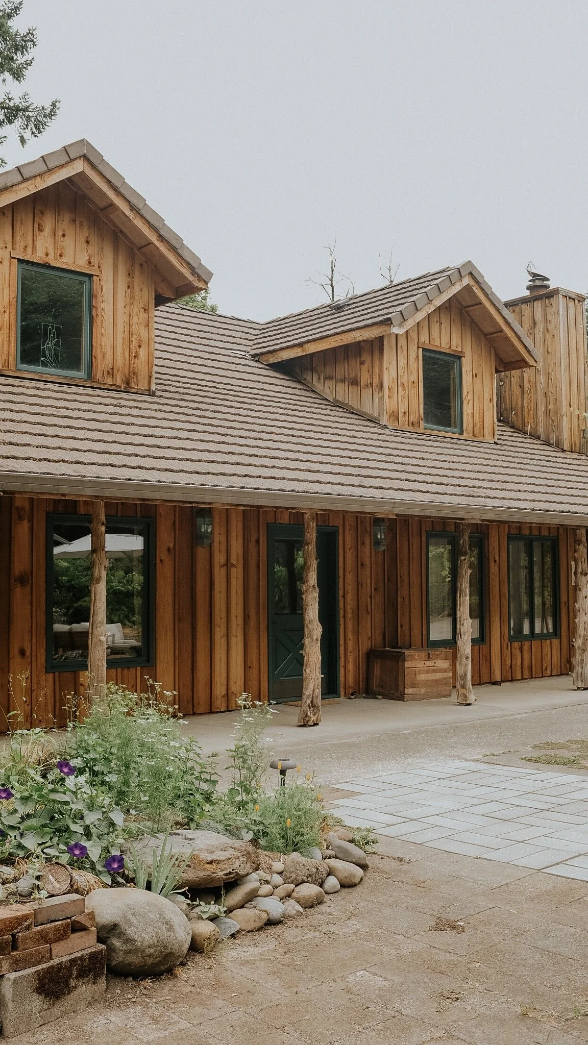 Deep Creek Farmstead's wood-sided vacation home with dormer windows, stone patio, and landscaped gardens near Portland, Oregon.