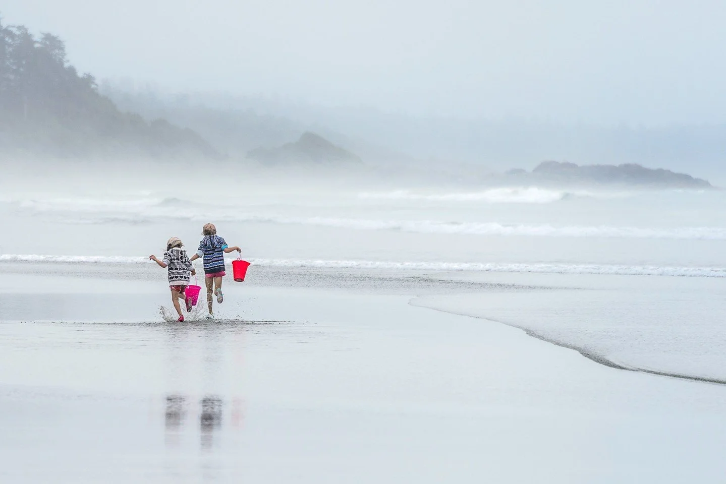 Tofino Girls - Jannik Plaetner - SCC / Everest Club 2023 Competition - Best of Show. 

Two children running joyfully toward the water on a misty beach, carrying colorful buckets with their reflections visible in the sand. 

#prpacanada #prpa #photogr