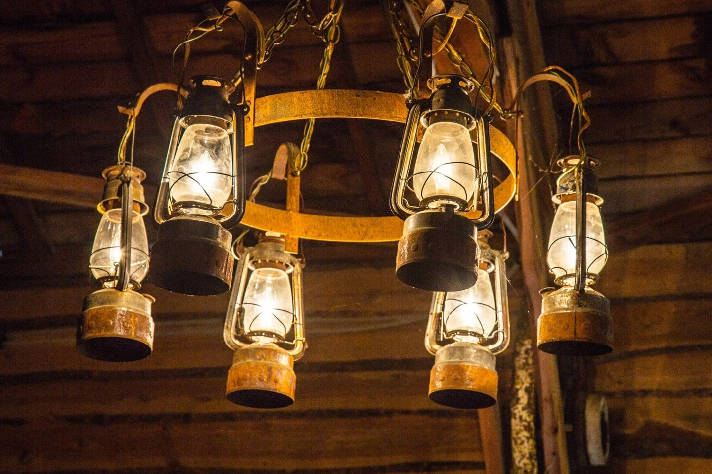 A rustic chandelier fashioned from vintage kerosene lanterns provides warm illumination within a cabin interior.

Lantern Lights - Larry Easton - RePC / Outing - Digital Image 2024 Competition - 2nd Place.

#prpacanada #prpa #photography #prairie