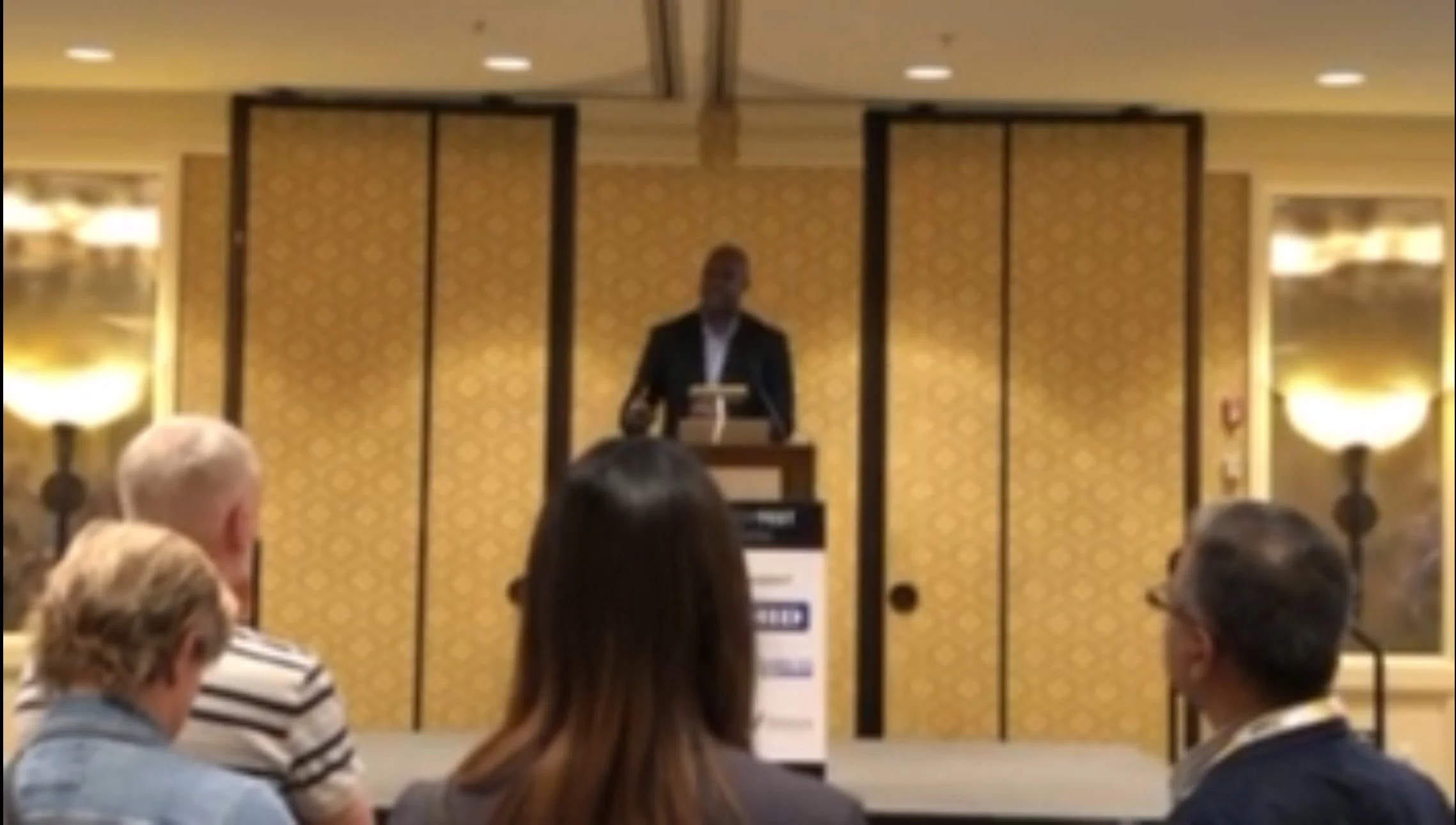 Speaker at podium addressing an audience in a conference room