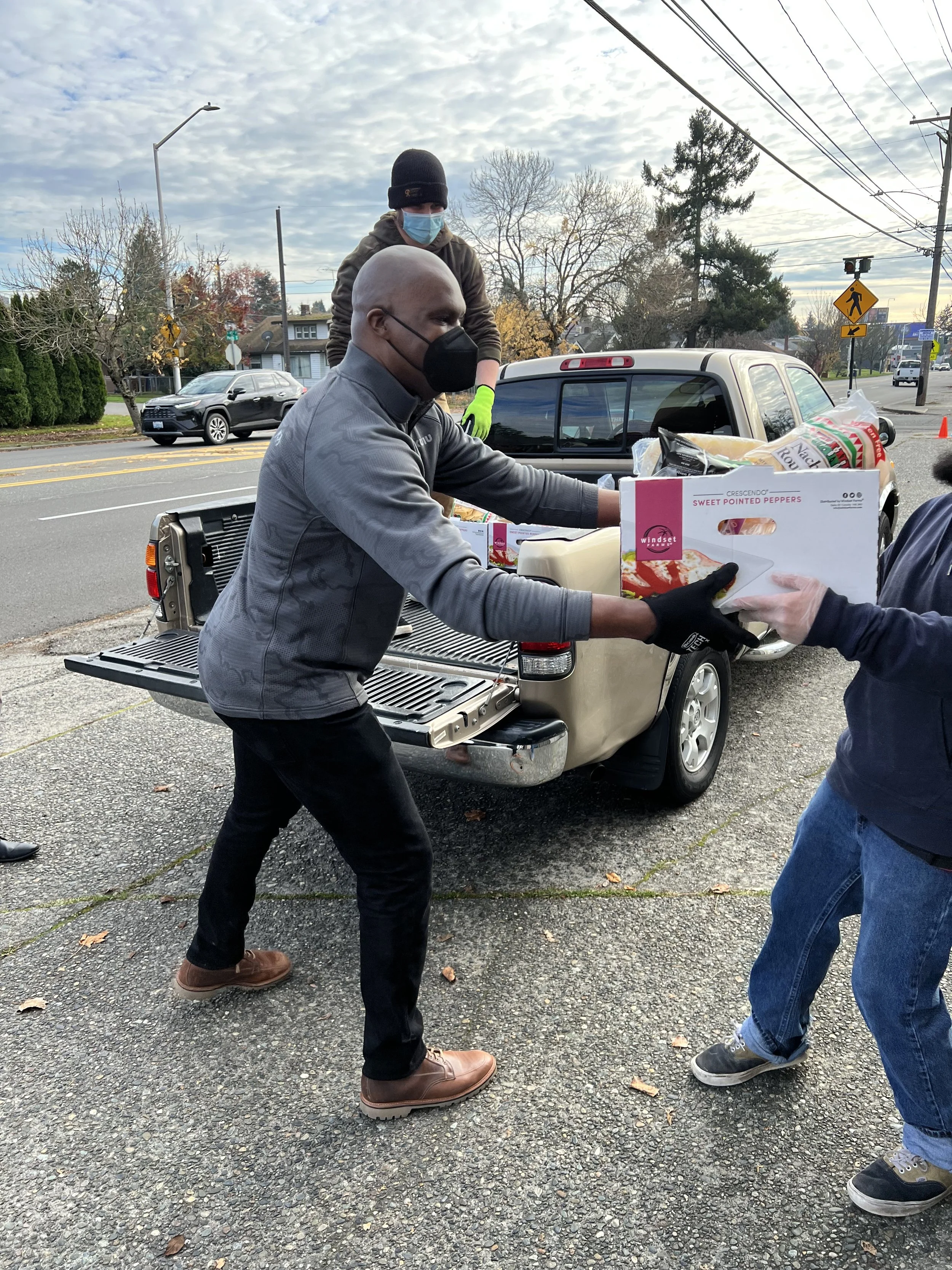 People wearing face masks and delivering boxes of food from the back of a pickup truck.