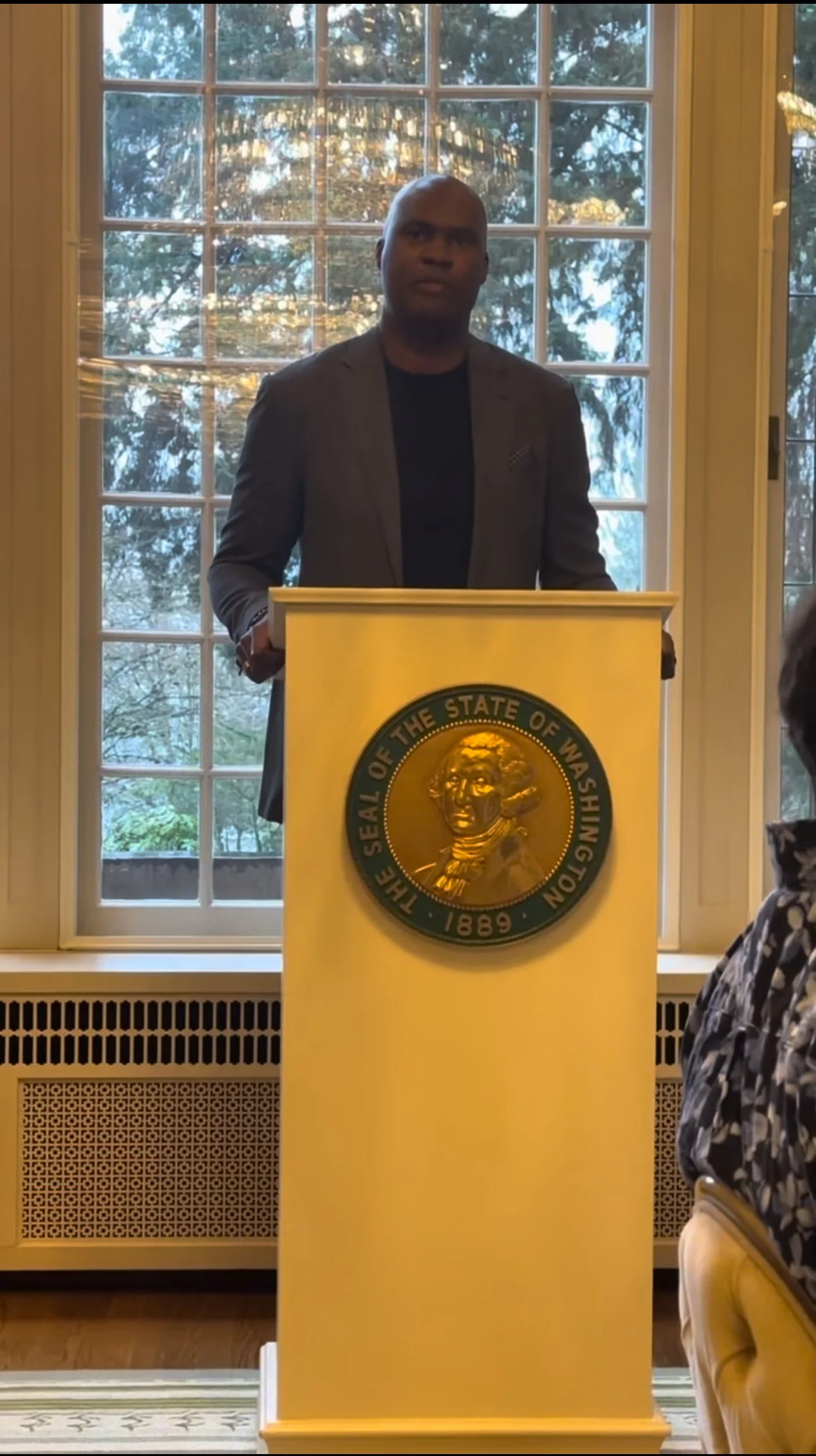 Man standing at a podium with the Seal of the State of Washington