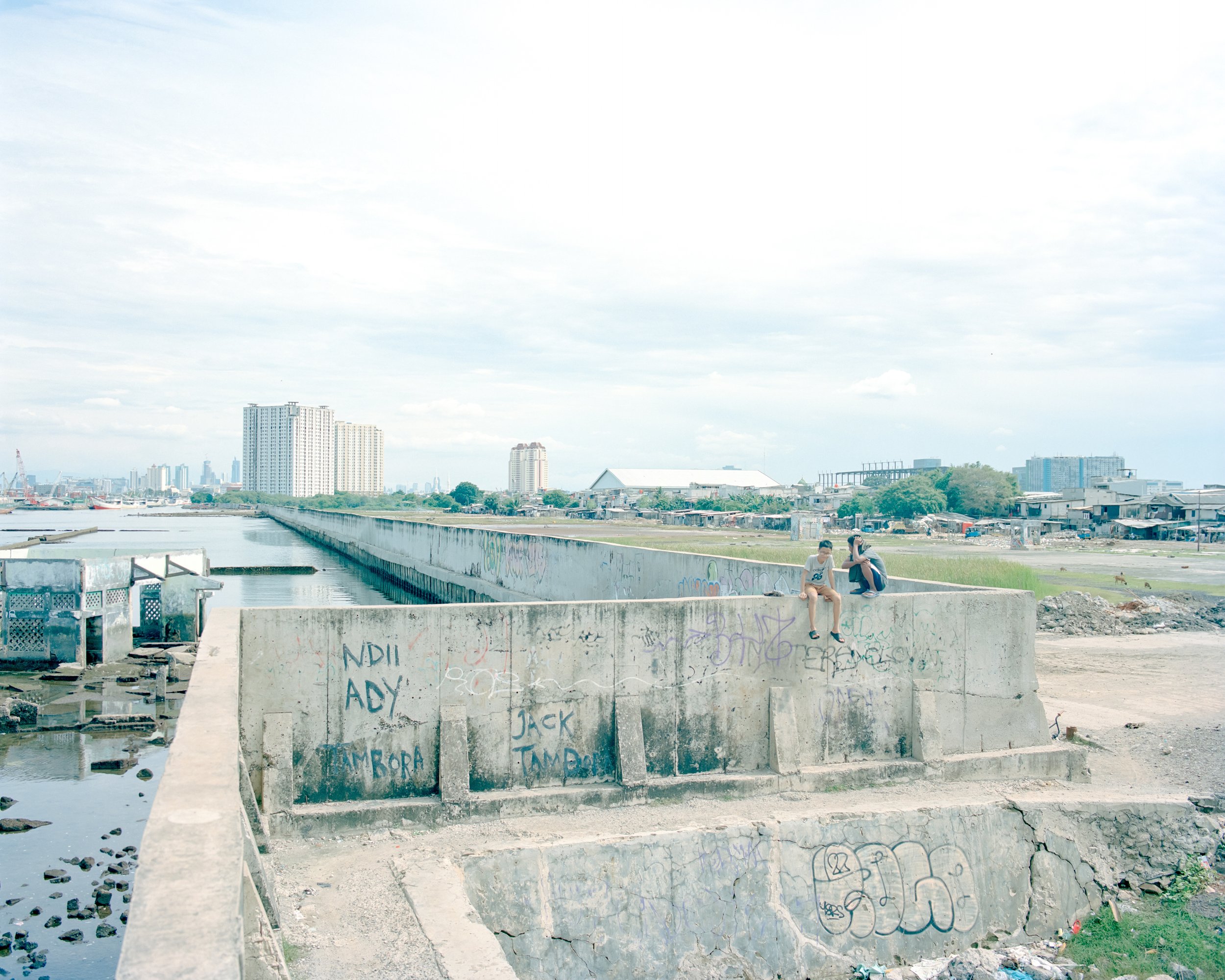 Boys who are relaxed on the seawall near an abandoned mosque that has already drowned at high sea level in the Muara Baru district, Jakarta (Indonesia, Jakarta, 2025)