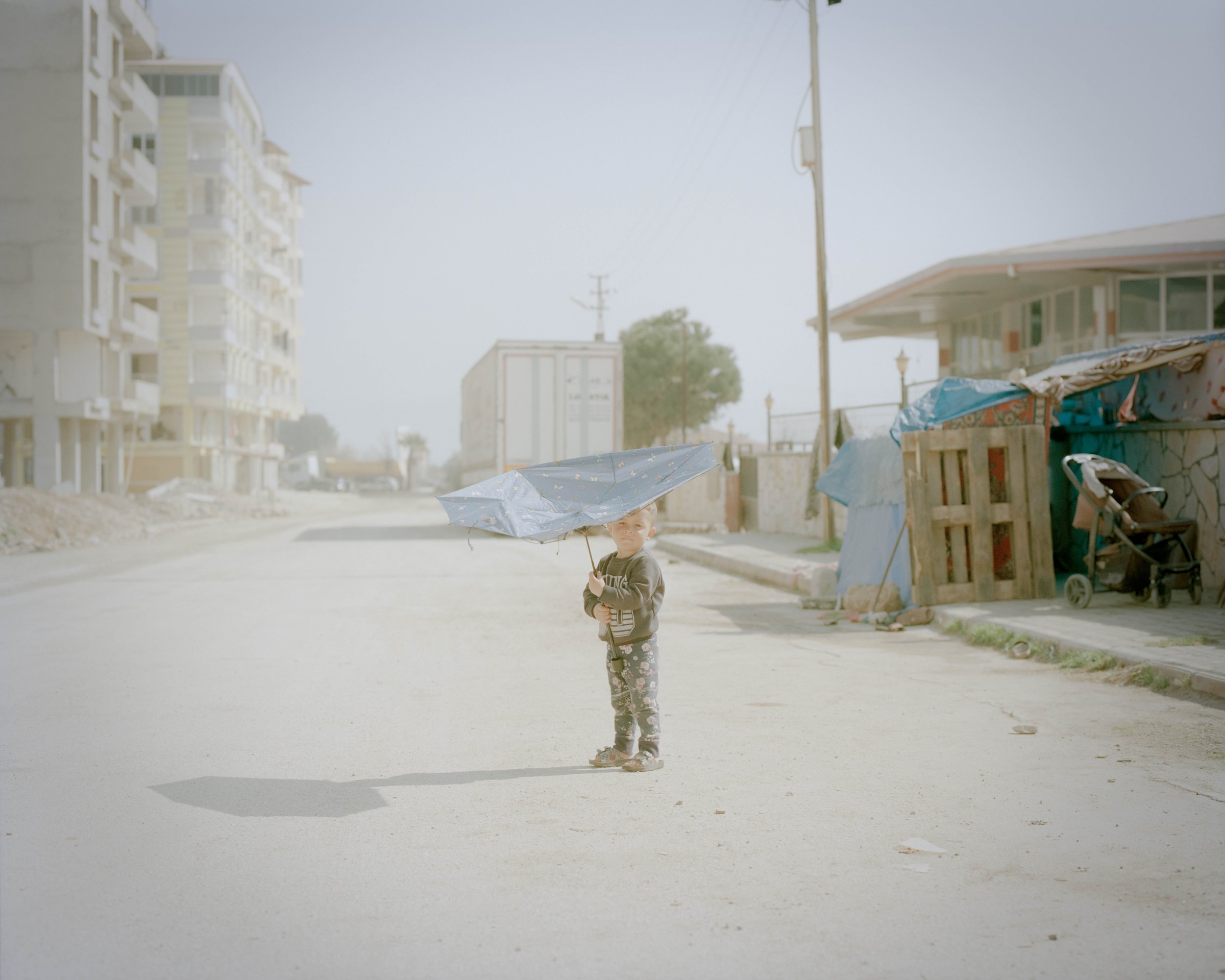 A Syrian refugee boy with a broken umbrella.