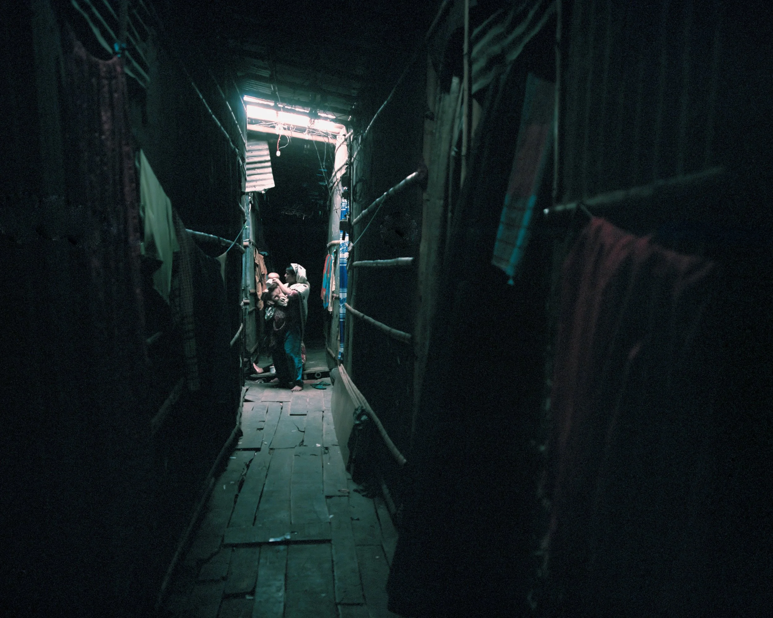 A mother, a climate migrant from Bhola Island, is caring for her baby in a muggy, narrow, dimly lit room in the Jhilpar slum.
Many migrants, mainly from southern coastal areas such as Bhola, Barishal, and Kuakata, reside in this slum.
Many migrants t