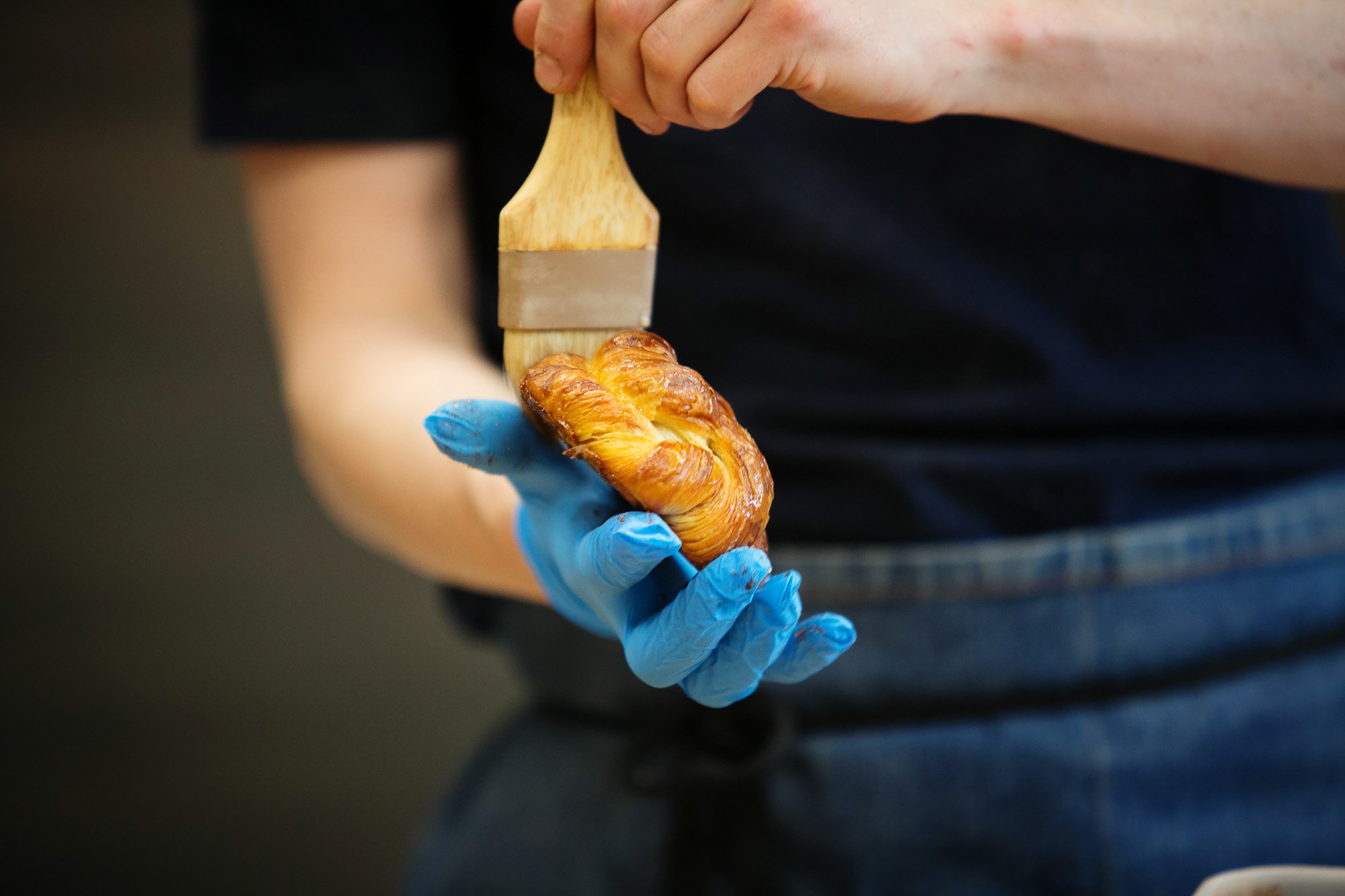 Artisan baker glazing a croissant with a brush.jpg