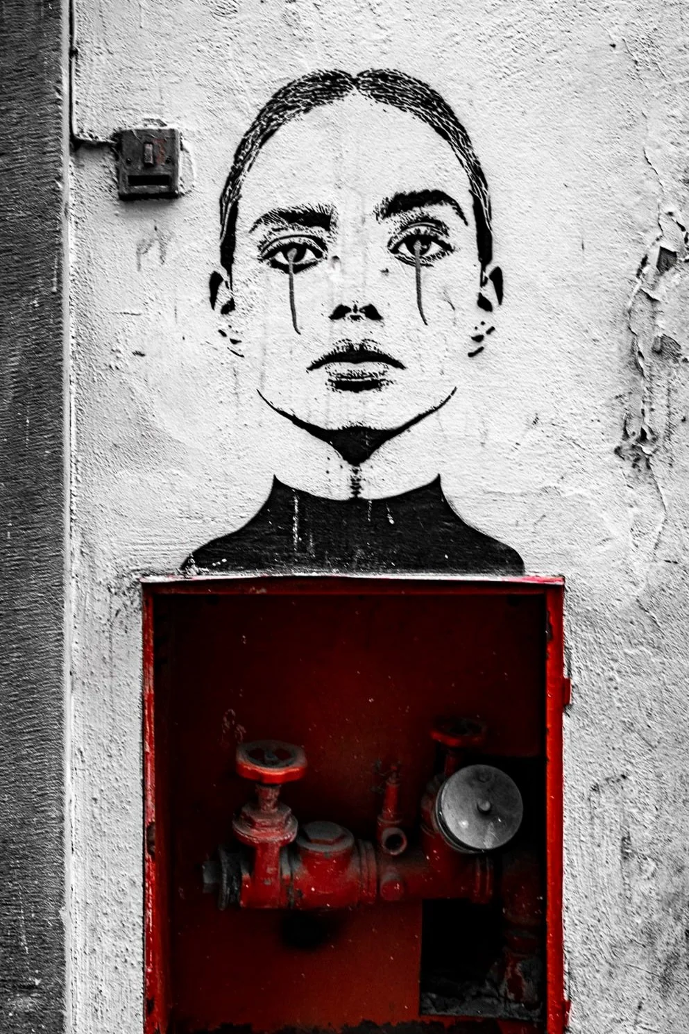 alexander_prior_photographer_vancouver_woman's face with tears on a textured wall, positioned above a red fire hose cabinet.