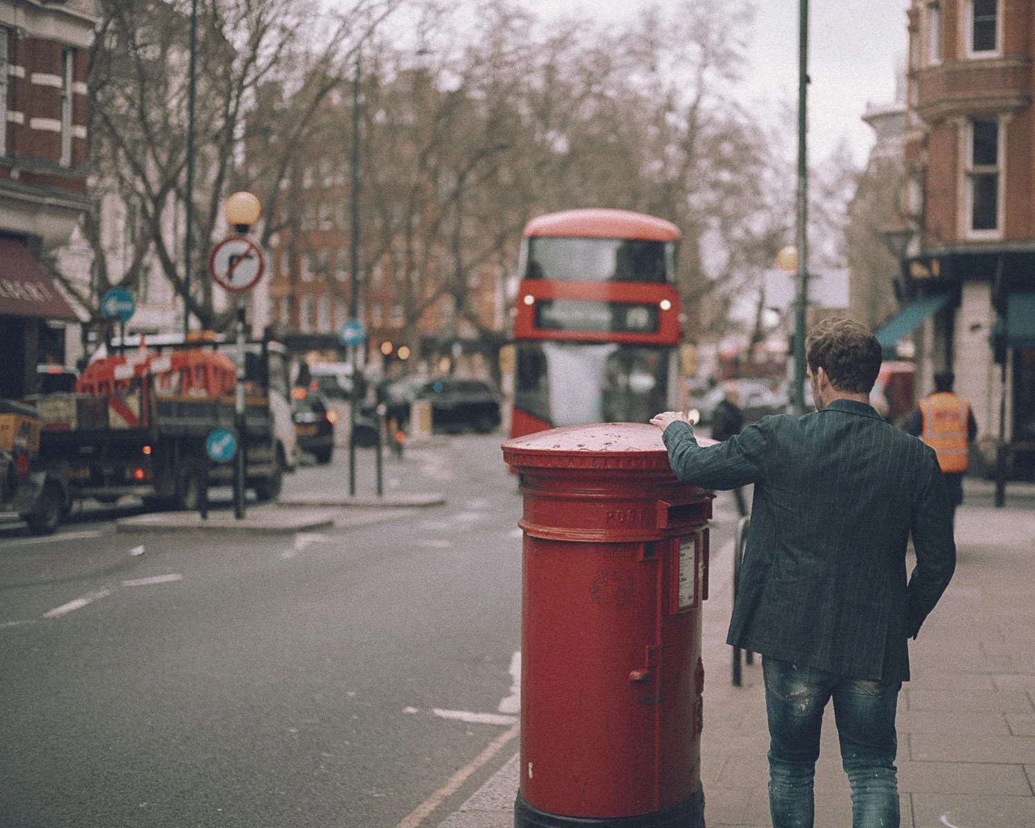 alexander_prior_photographer_vancouver_A man in a dark denim jacket and jeans is standing next to a red mailbox on a london city street.