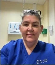 Head-and-shoulders photo of a Health Liaison Team member wearing blue clinical scrubs, photographed in a clinical setting.