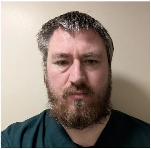 Head-and-shoulders photo of a Health Liaison Team member wearing clinical scrubs, facing the camera against a plain indoor background.