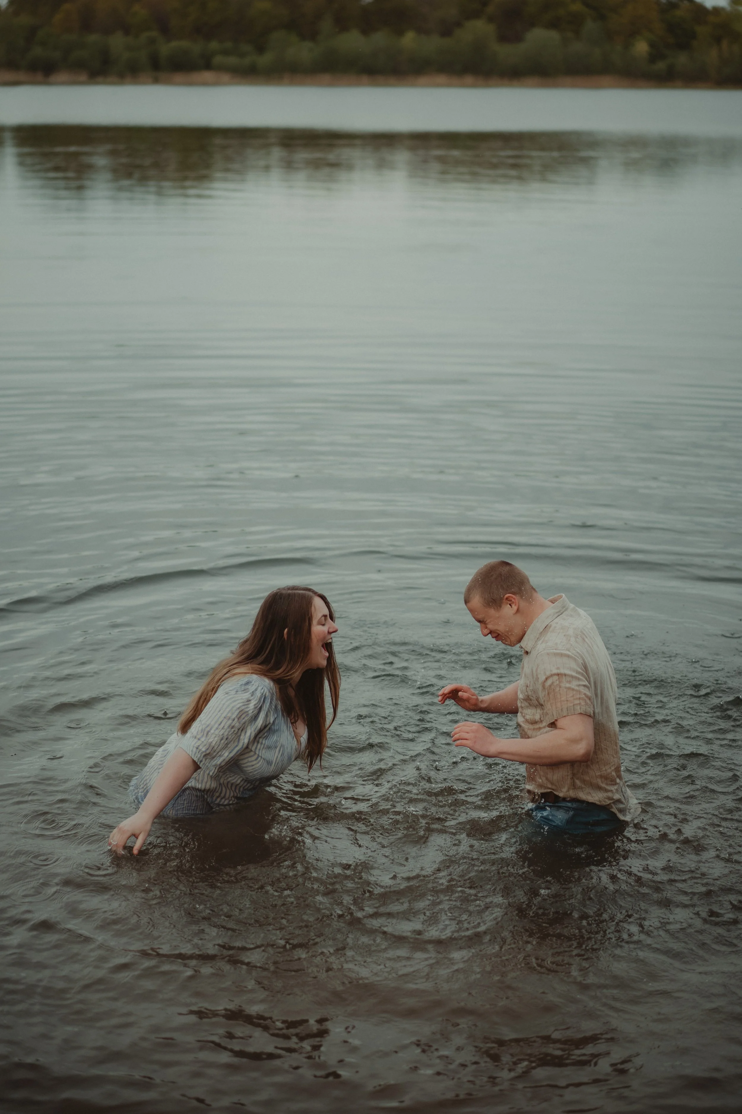 Couple having fun dressed up in the water, splashing each other during their pre-wedding photo session