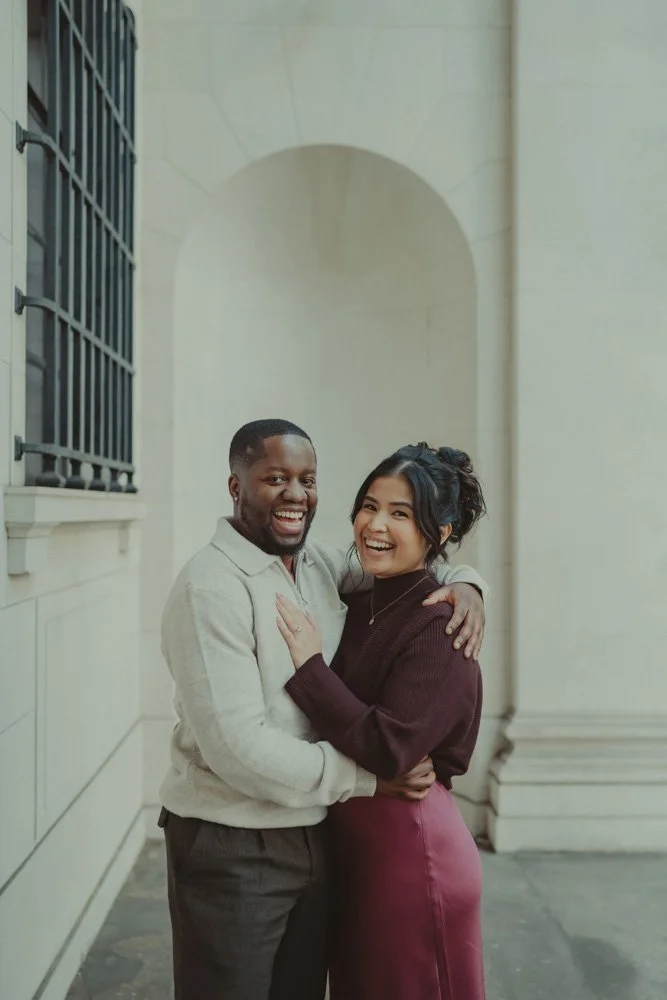Couple laughing and looking at the camera, at a save the date pre-wedding session in London, UK