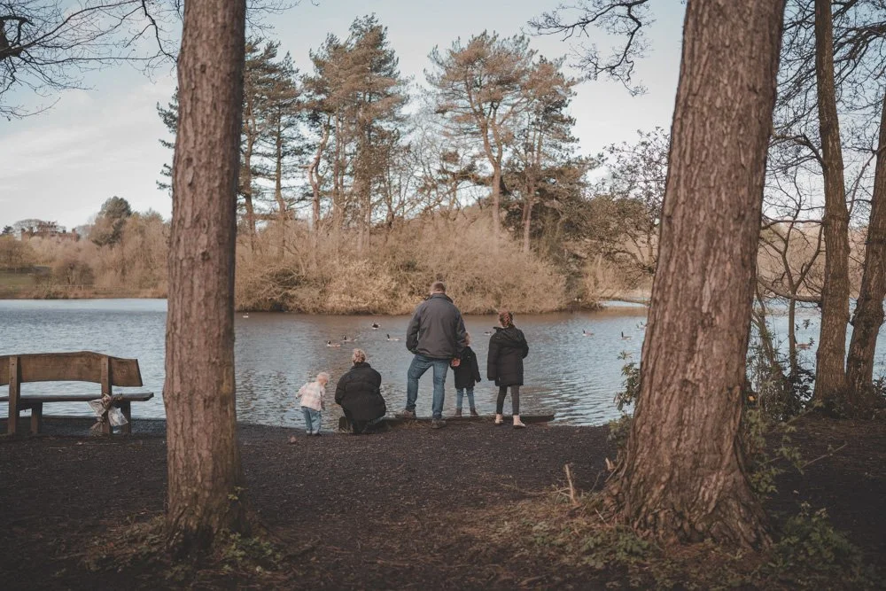 Family photographed from far behind in front of the lake at Cuerden Valley Park