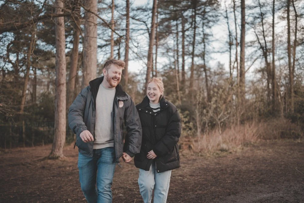 Boyfriend and girlfriend walking towards the camera and laughing, in the woods of Cuerden Valley Park