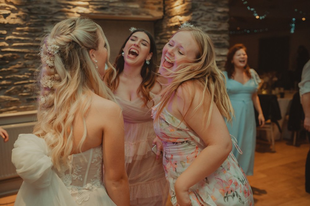 Bride and bridesmaids singing and dancing together on the dancefloor of Gwesty'r Emlyn Hotel in Newcastle, Wales
