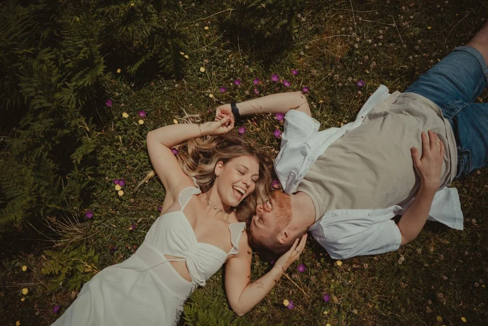 Young couple laying on the grass and laughing, at a pre-wedding photoshoot in Wales