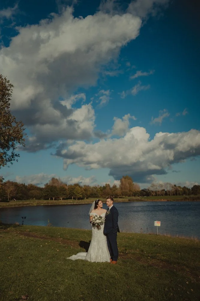 Bride and groom photographer from afar, near a lake, on the grounds of The Waterfront Barton Marina