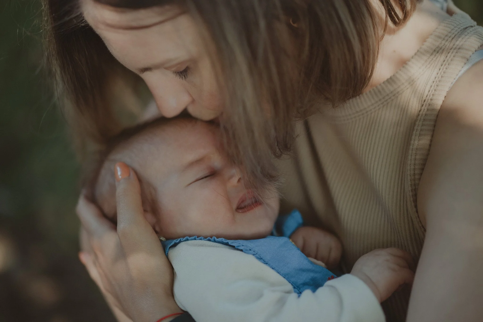Portrait of mother kissing her newborn's baby forehead