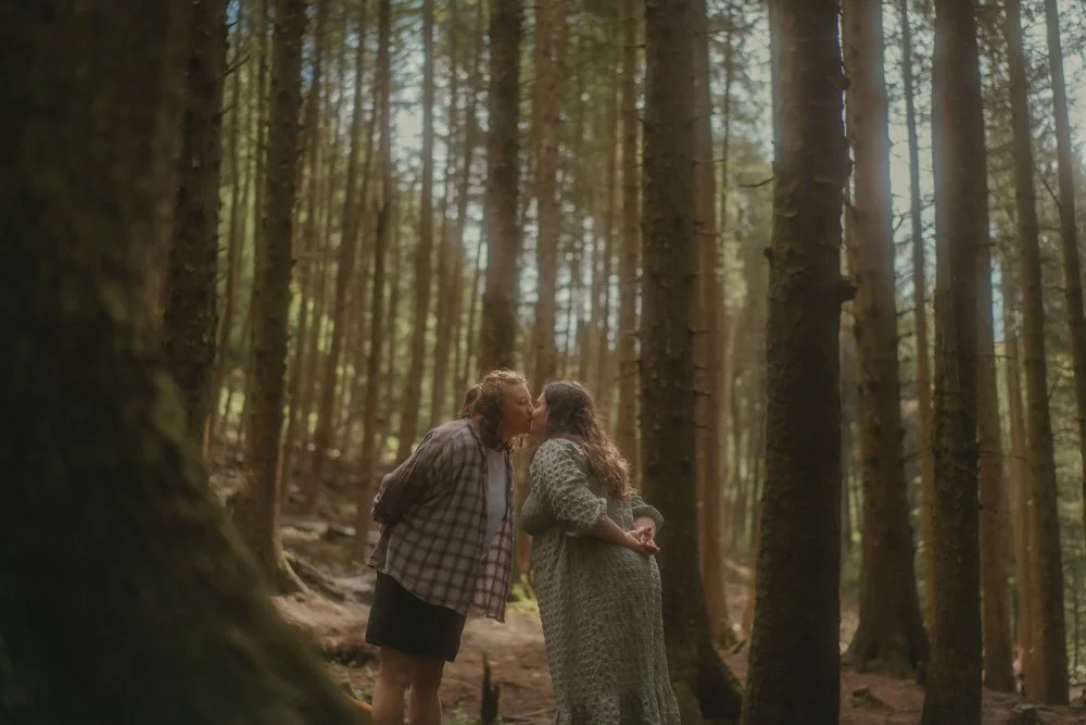Large landscape portrait of a LGBTQ couple, kissing, in the middle of the woods at Snake Woodland