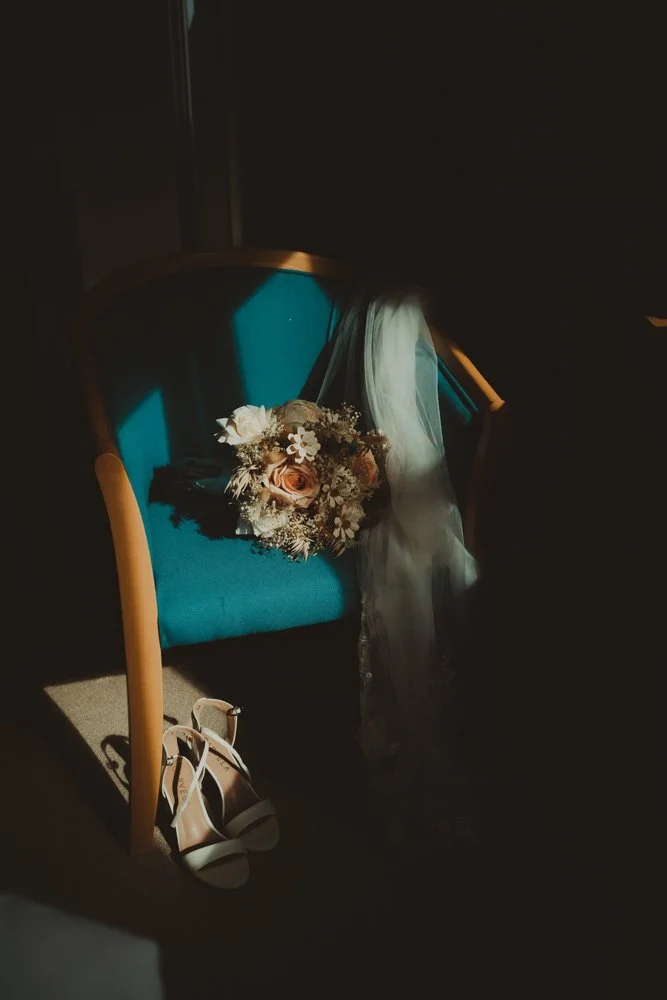 Low light photography of wedding flowers and shoes, on a blue chair, at Gwesty'r Emlyn Hotel in Newcastle, Wales