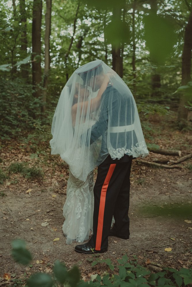 Full body photo of groom in military outfit and bride, kissing under the veil in Basingstoke, UK
