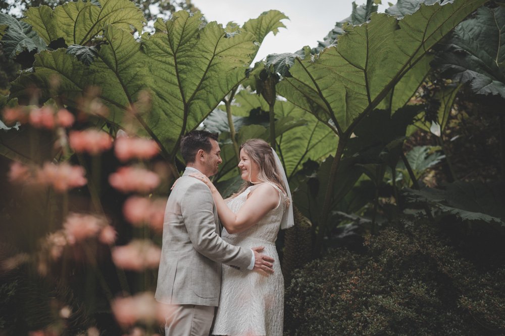 Bride and groom holding each other under some big plants in Clyne Gardens, Swansea