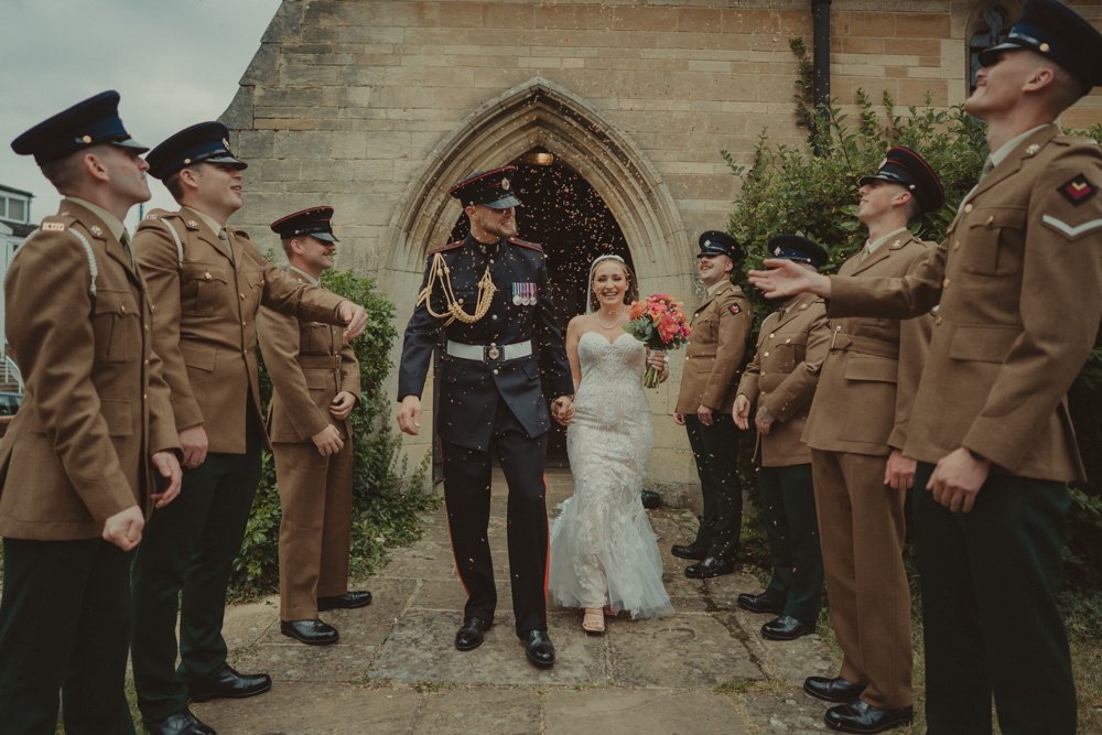 Bride and groom walking out the church for a confetti exit, with military people first in the row, in Basingstoke, UK