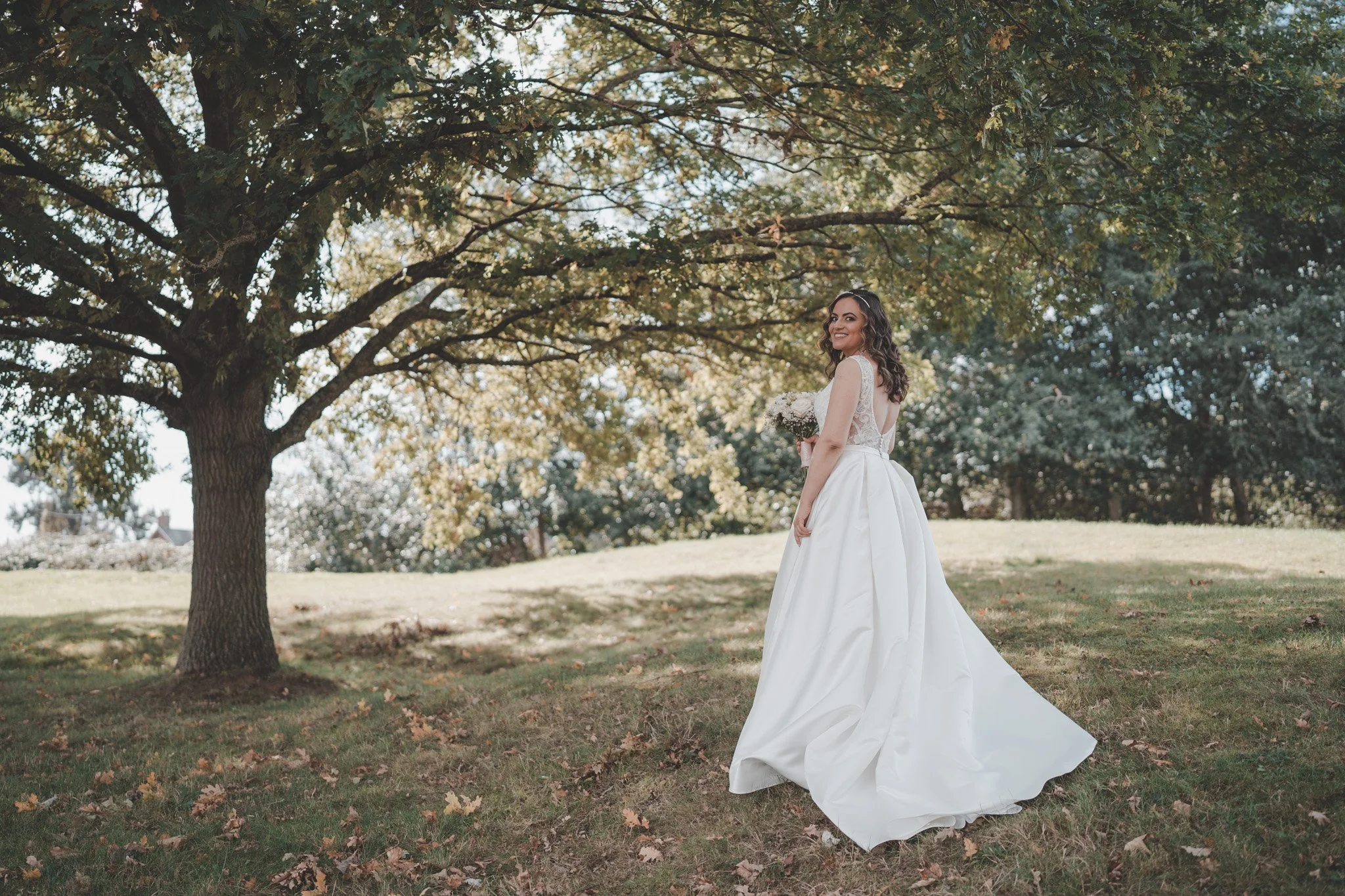 Bride posing for the camera under a tree on her wedding day, in front of Delta Hotels by Mariott Northampton