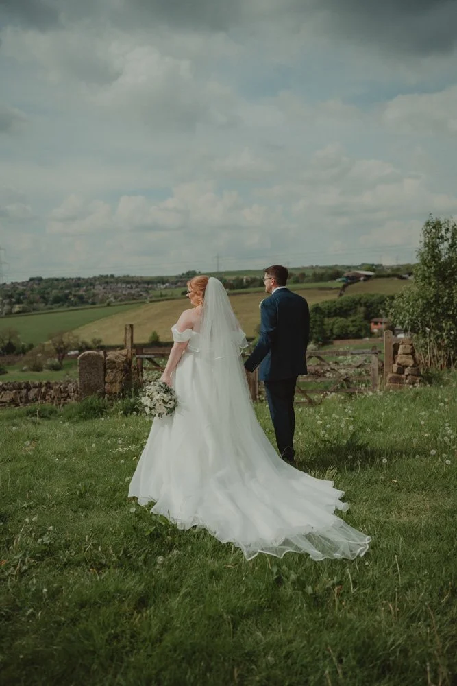 Bride and groom walking on a field with their backs to the camera during the couple photoshoot, at The White Hart Inn at Lydgate
