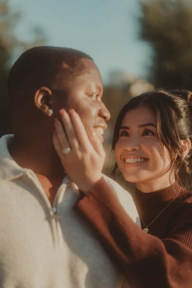 Portrait of engaged couple, girl holding her hand on her boyfriend's cheek, and you can see the engagement ring, at a pre-wedding photoshoot in London