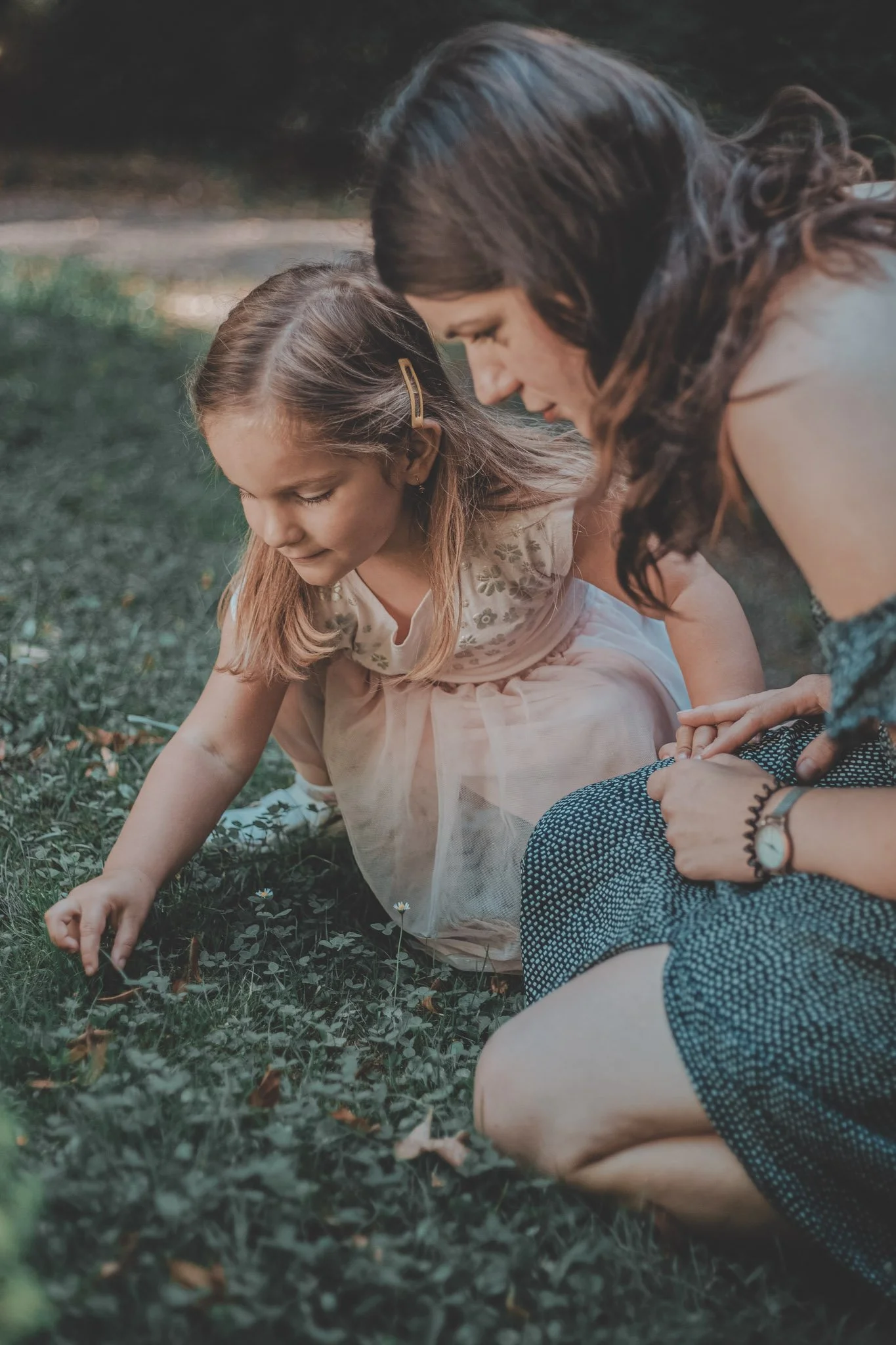 Mother and her young daughter looking at something in the grass during a mother and daughter photoshoot