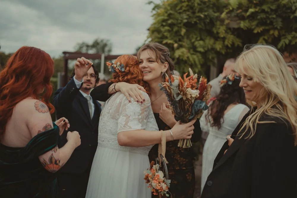 Bride hugging a friend, surrounded by wedding guests at her wedding, at The Chester Fields Country Pub, Restaurant & Wedding Venue, UK