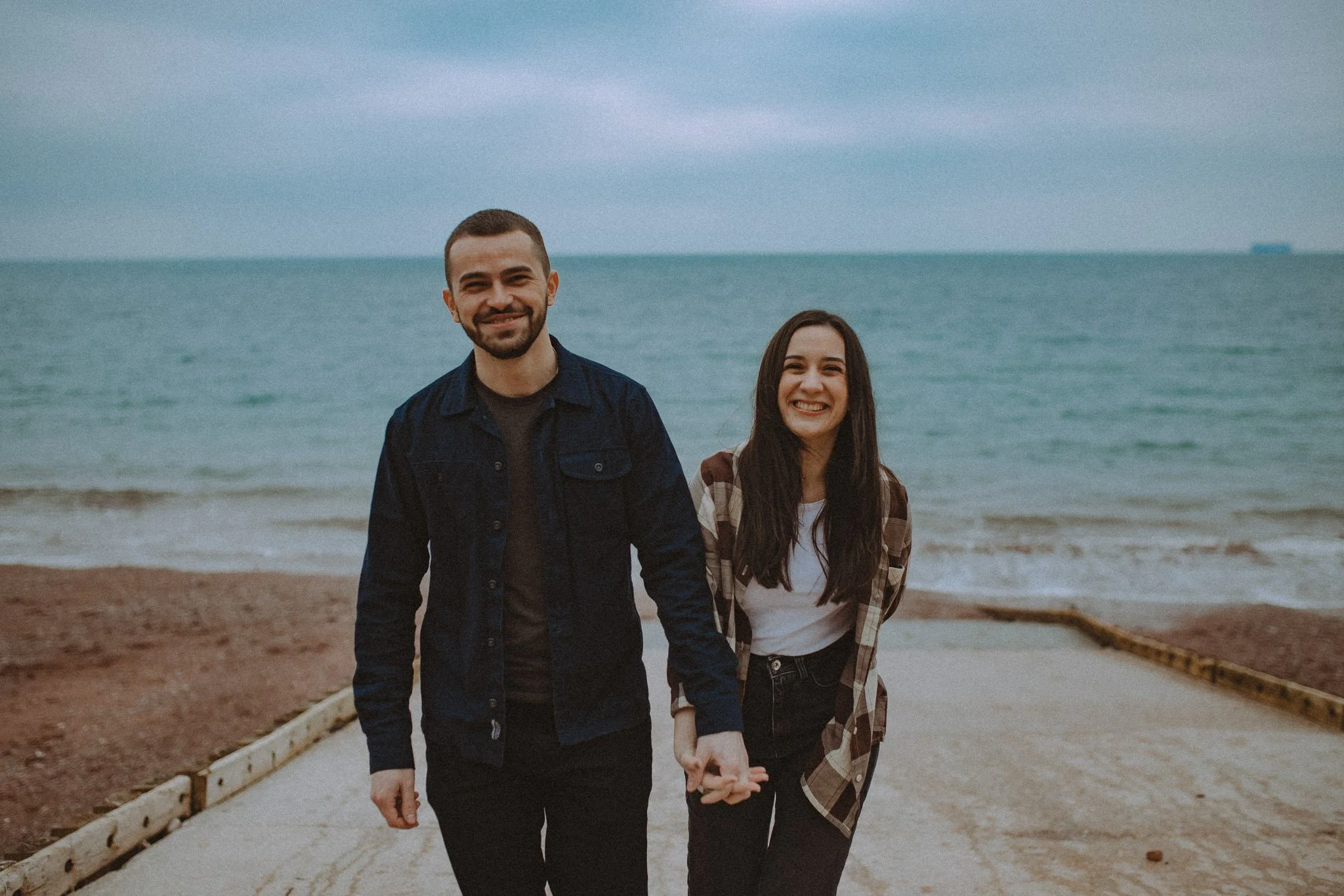 Couple holding hands and smiling at the camera on Oodicombe beach in Torquai