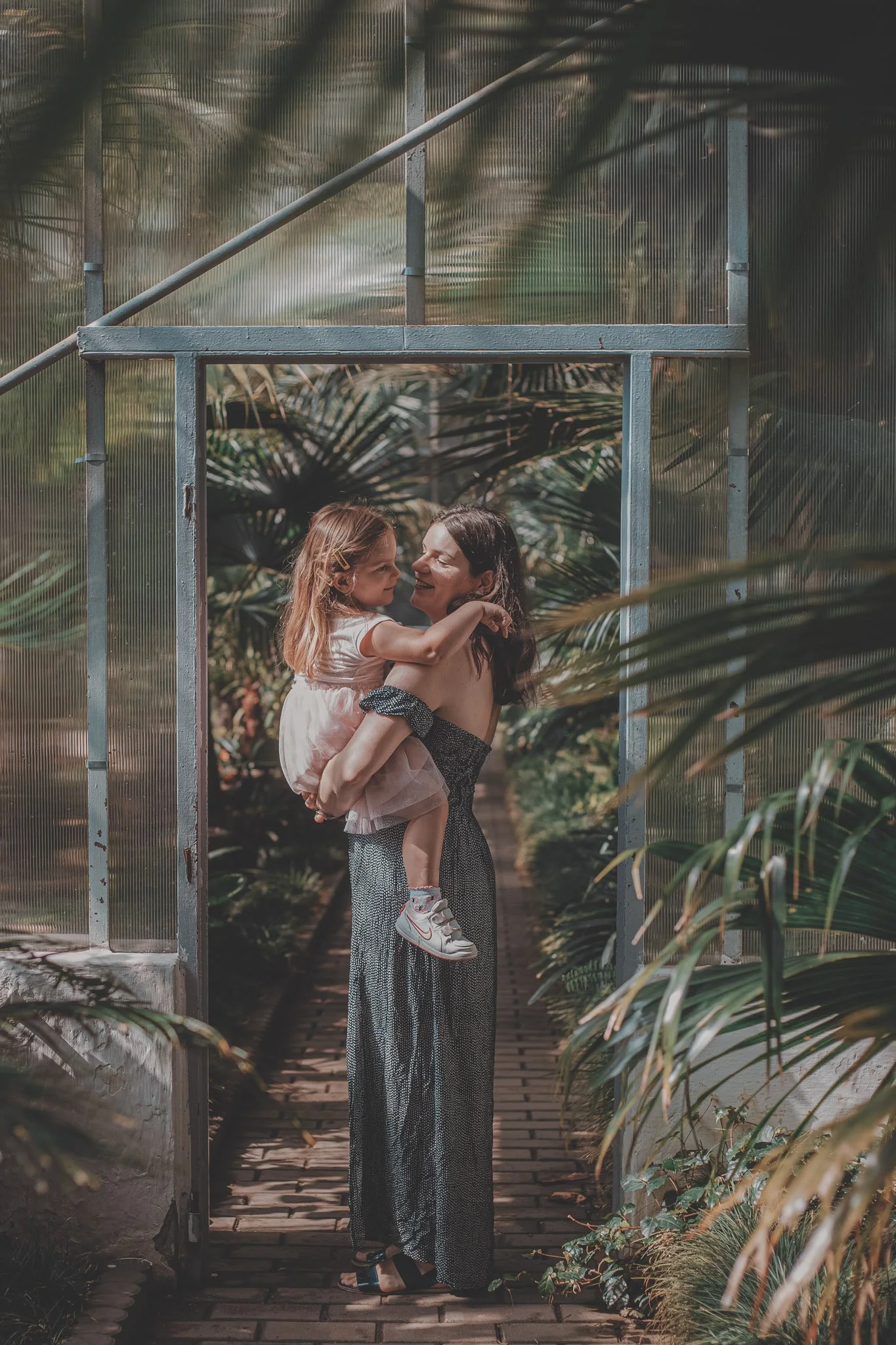 Young mom holding her daughter in her arms, in a botanical garden during a mommy & me photoshoot