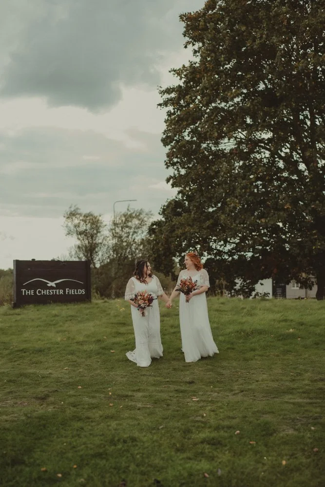 Two brides walking and holding hands on the grounds of The Chester Fields Country Pub, Restaurant & Wedding Venue, UK