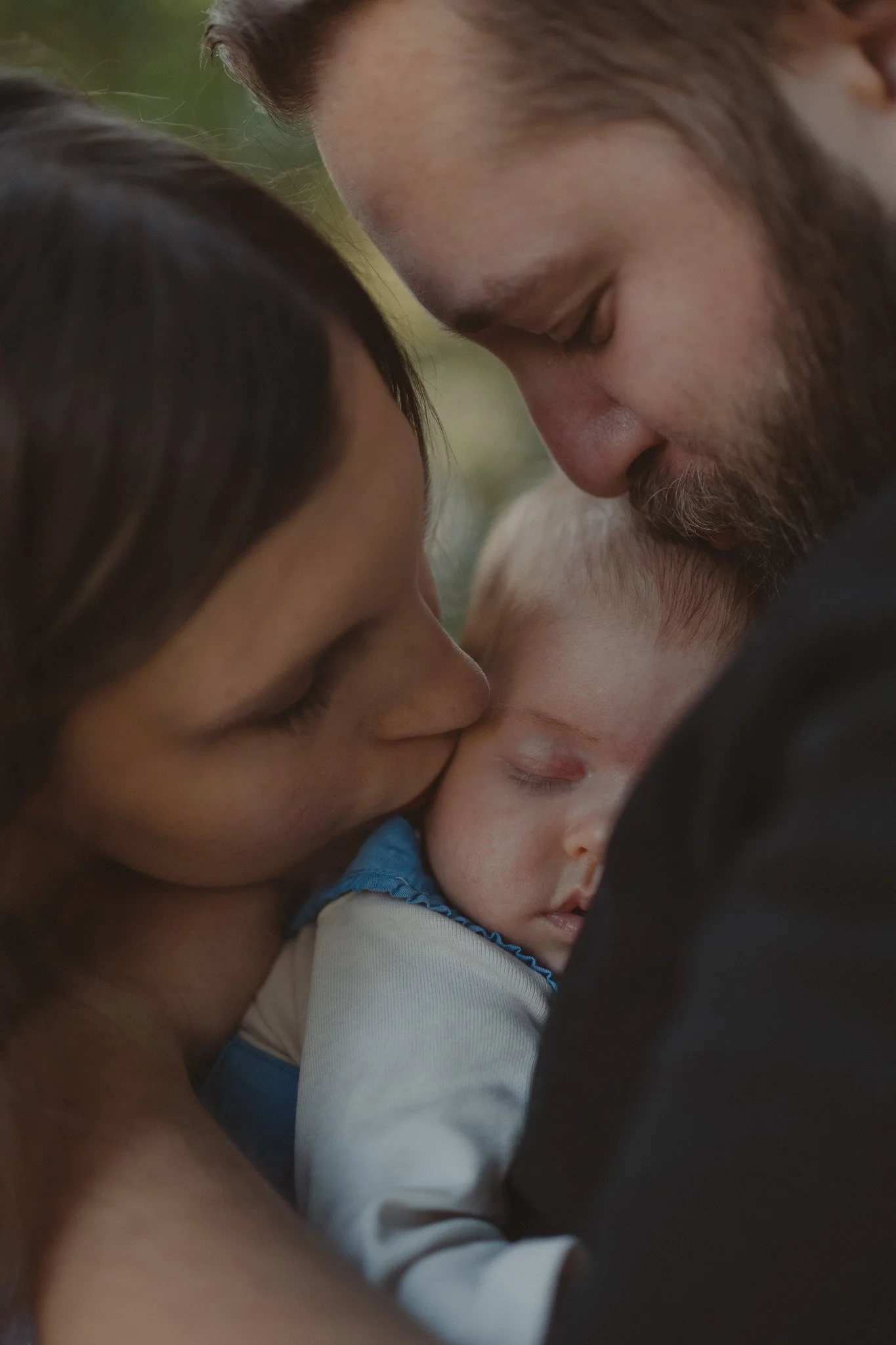 Close-up portrait of parents kissing their child during a newborn family photoshoot