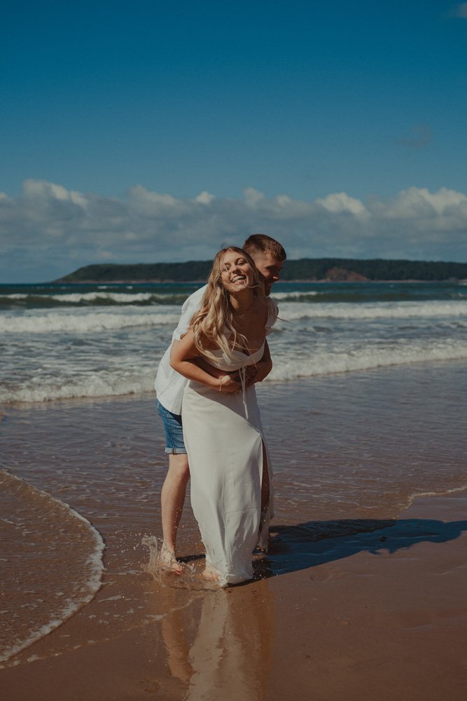 Young couple laughing and holding together at their save the date photo session, on the beach of Three Cliffs Bay, Wales