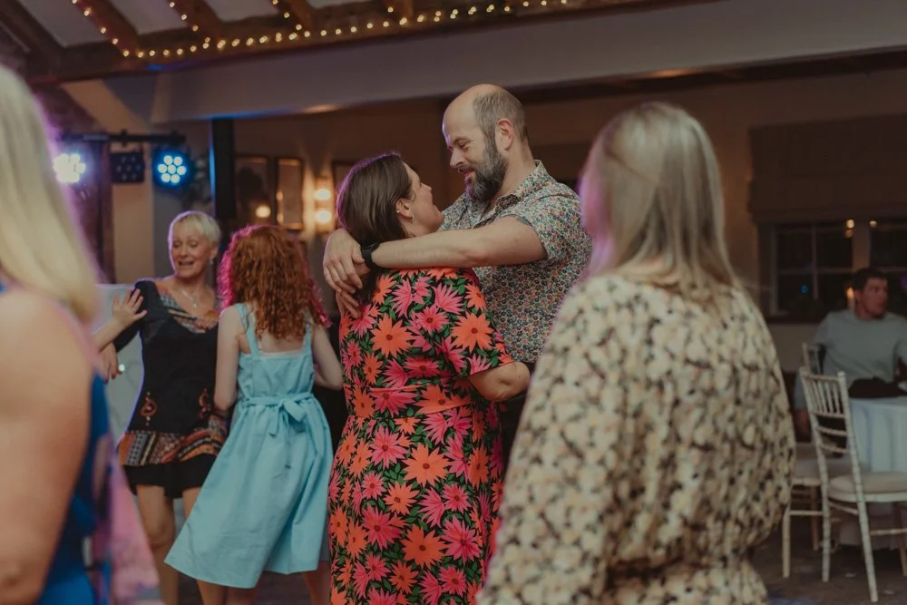 Two wedding guests photographed holding and dancing together at a wedding at The Waterfront Barton Marina