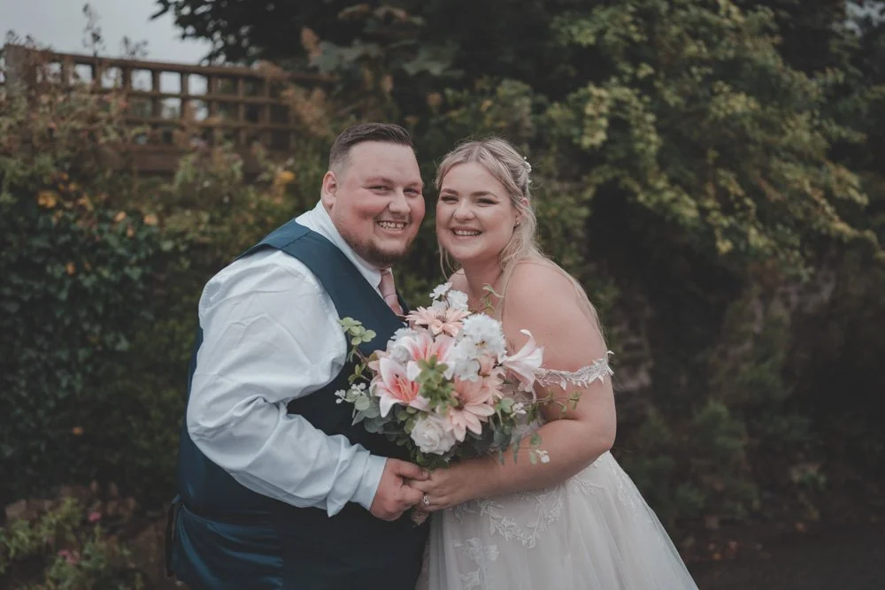 Bride and groom smiling at the camera on their wedding day, in Wales, UK