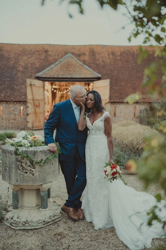 Vertical wedding portrait of groom kissing his wife's forehead, in front of a barn in blue hour, in Drayton, Oxfordshire 