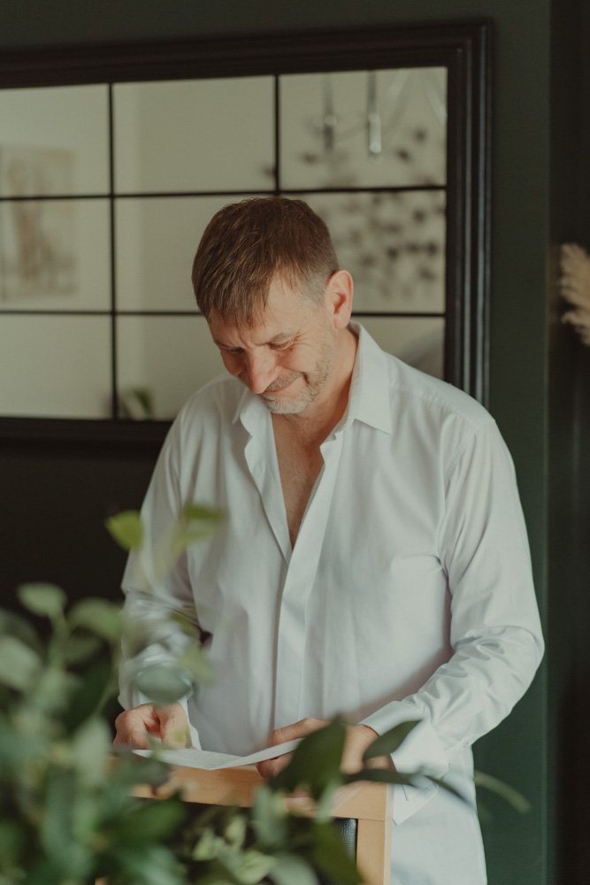 Man smiling while reading a letter of his future bride on the morning of his wedding, in Swadlincote, UK